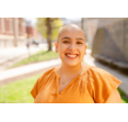 Natalie's headshot, standing outside on a sunny day in an orange top and smiling.